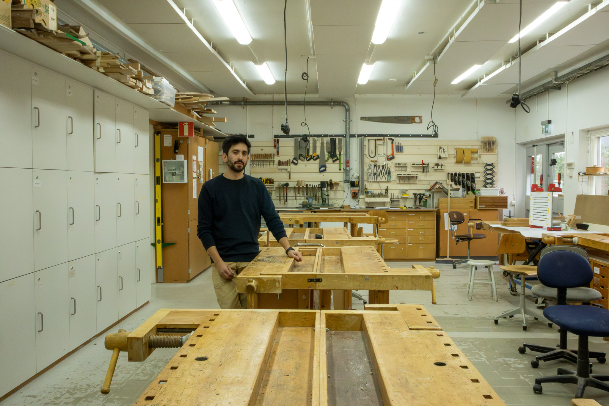 En man i blå tröja står i en lokal med ett flertal arbetsbänkar i trä